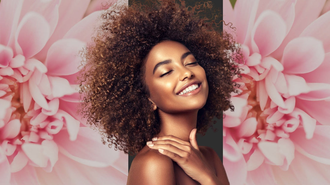 Strahlende Frau mit natürlichem Glow und geschlossenen Augen vor rosa Blütenhintergrund – symbolisiert pure, moderne und bewusste Hautpflege im Clean-Beauty-Kontext.